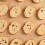 Crostini slices arranged on parchment-lined baking sheet