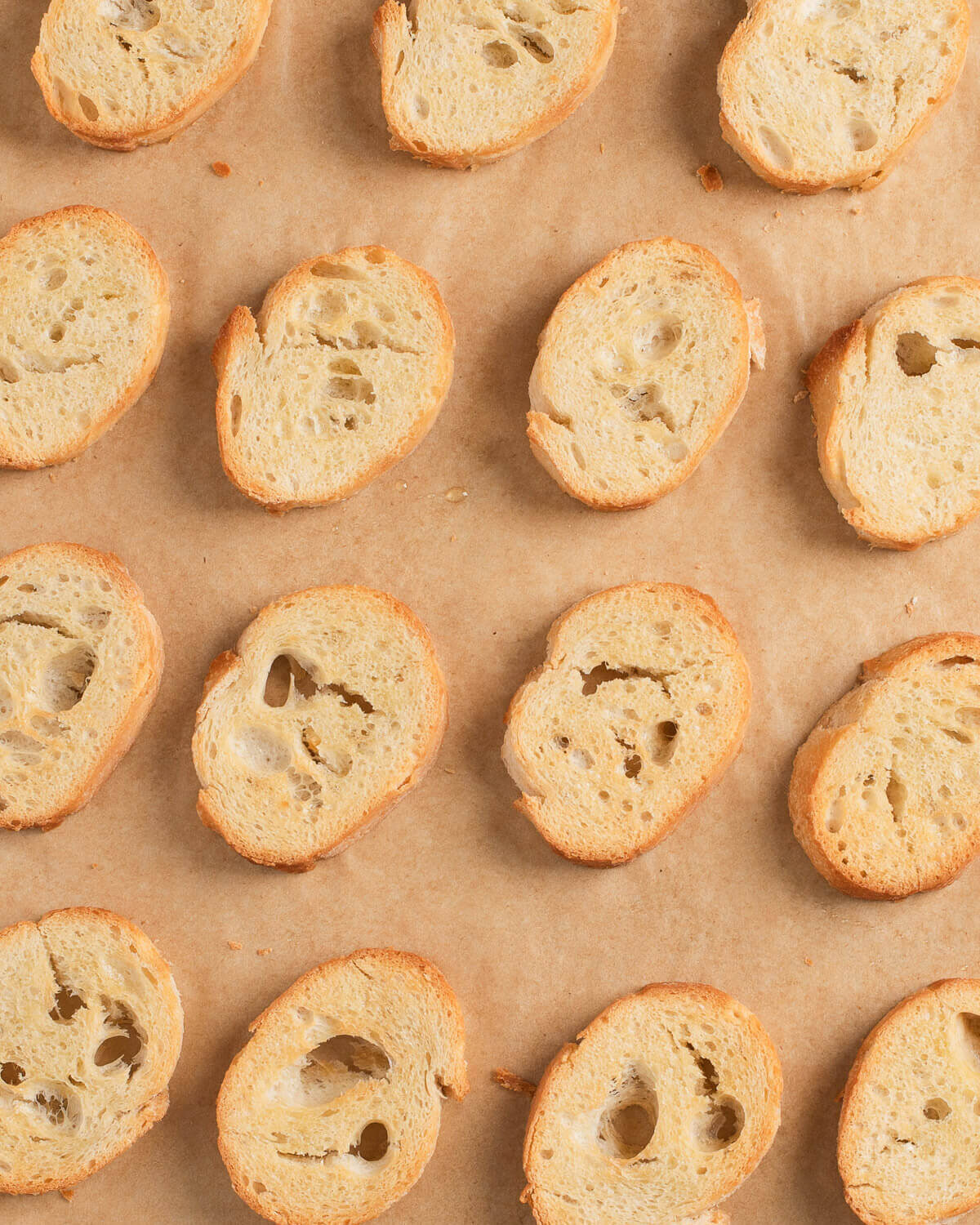 Crostini slices arranged on parchment-lined baking sheet