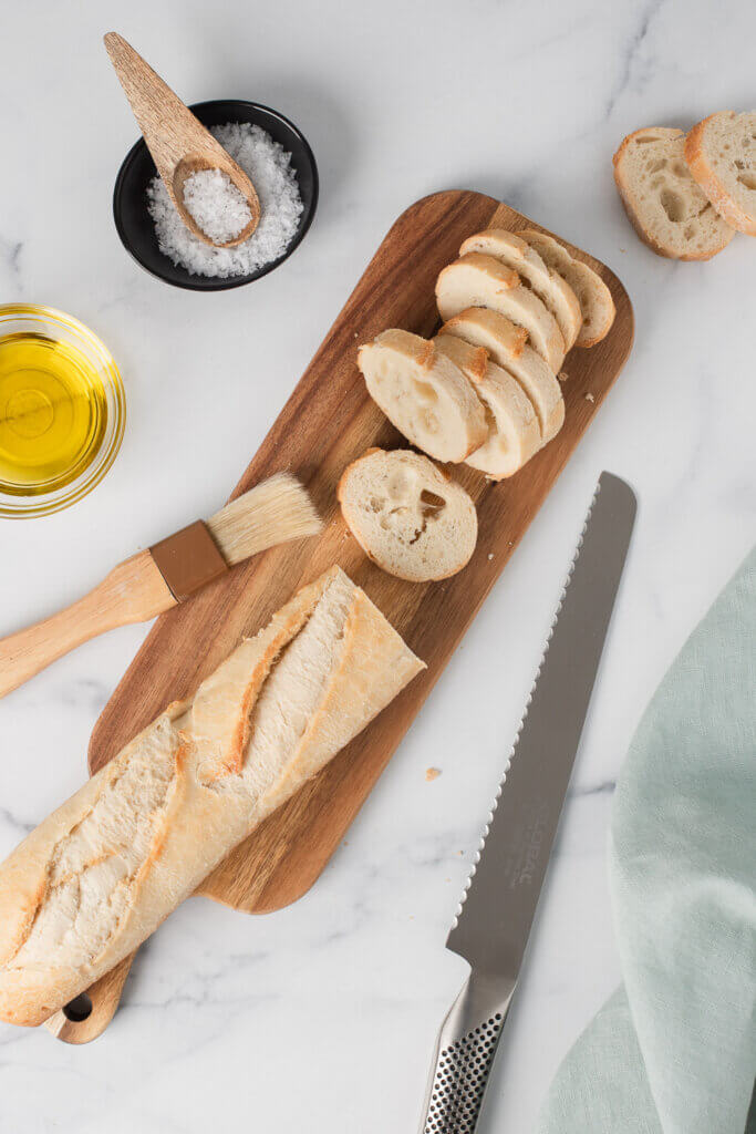 Baguette sliced on a cutting board with olive oil, salt, and serrated knife