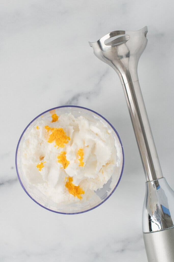 Ricotta cheese and citrus zest in a glass mixing bowl before blending with an immersion blender.