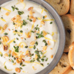 Creamy whipped ricotta garnished with chopped walnuts and herbs and served alongside slices of toasted bread.