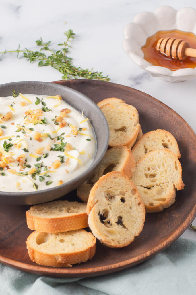 Bowl of whipped ricotta garnished with herbs and served with toasted bread slices.