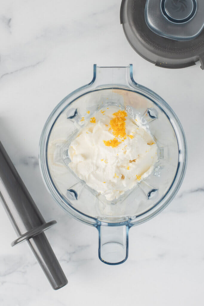 Ricotta cheese and citrus zest in a glass mixing bowl before blending with a blender.